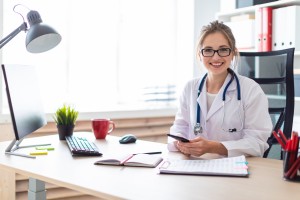 A beautiful young girl with glasses and a white coat is working in her office. On the neck of the girl hangs a stethoscope. photo with depth of field.